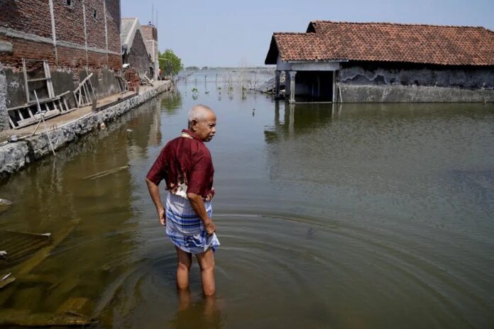 FILE - Sukarman walks on a flooded pathway outside his house in Timbulsloko, Central Java, Indonesia, July 30, 2022.