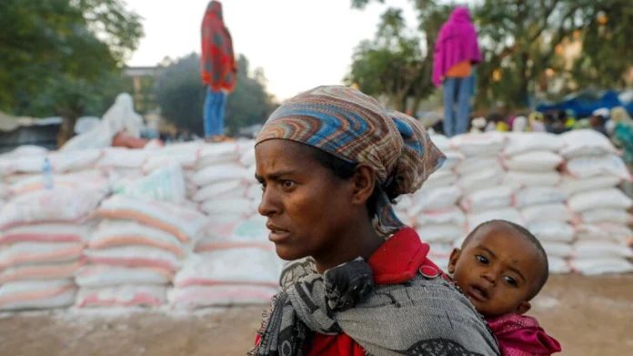 A woman carries an infant as she queues in line for food, at the Tsehaye primary school, which was turned into a temporary shelter for people displaced by conflict, in the town of Shire, Tigray region, Ethiopia on March 15, 2021. © Baz Ratner, Reuters